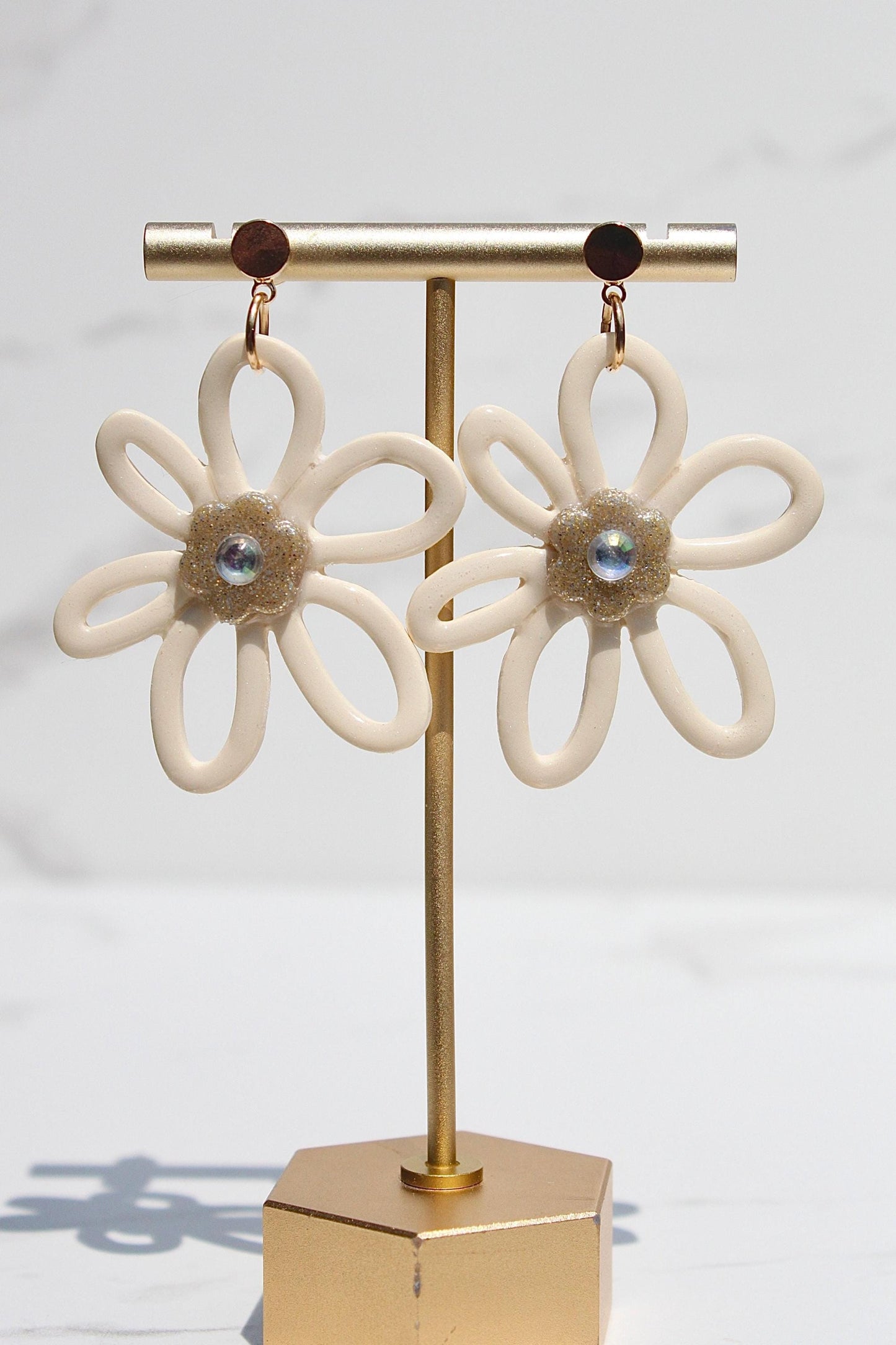 Pair of flower-shaped earrings on a gold stand against a white background