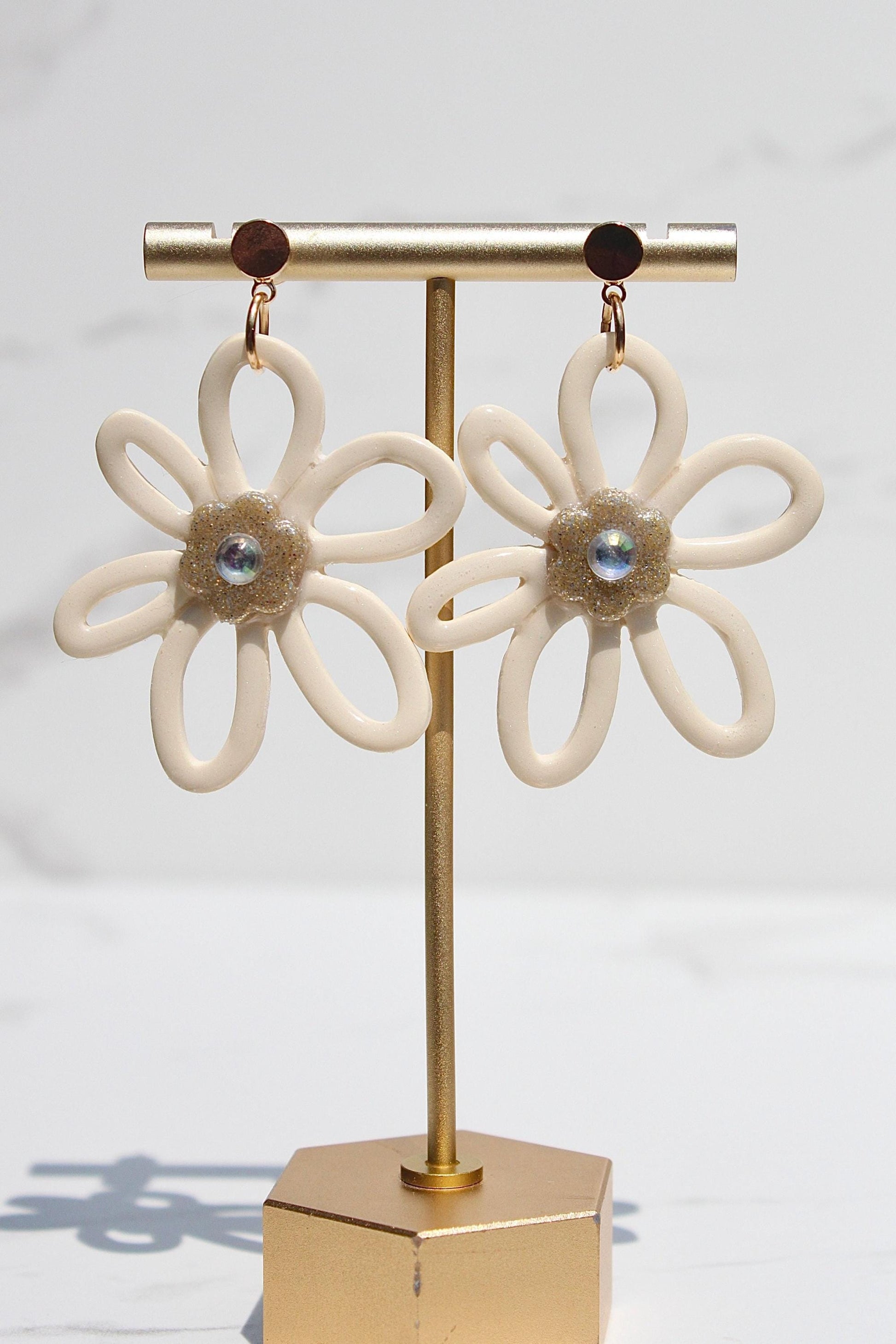 Pair of flower-shaped earrings on a gold stand against a white background
